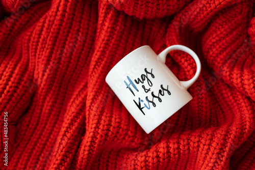 Hugs and kisses inscription on a white cup on a red knitted fabric. Love concept. St. Valentine's Day.