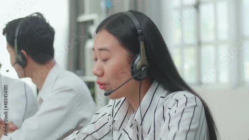 A Woman Of Three Asian Call Center Agents Wearing Headset Speaking To Customer On The Call While Two Of Her Colleagues Are Talking During Working At The Office
 photo