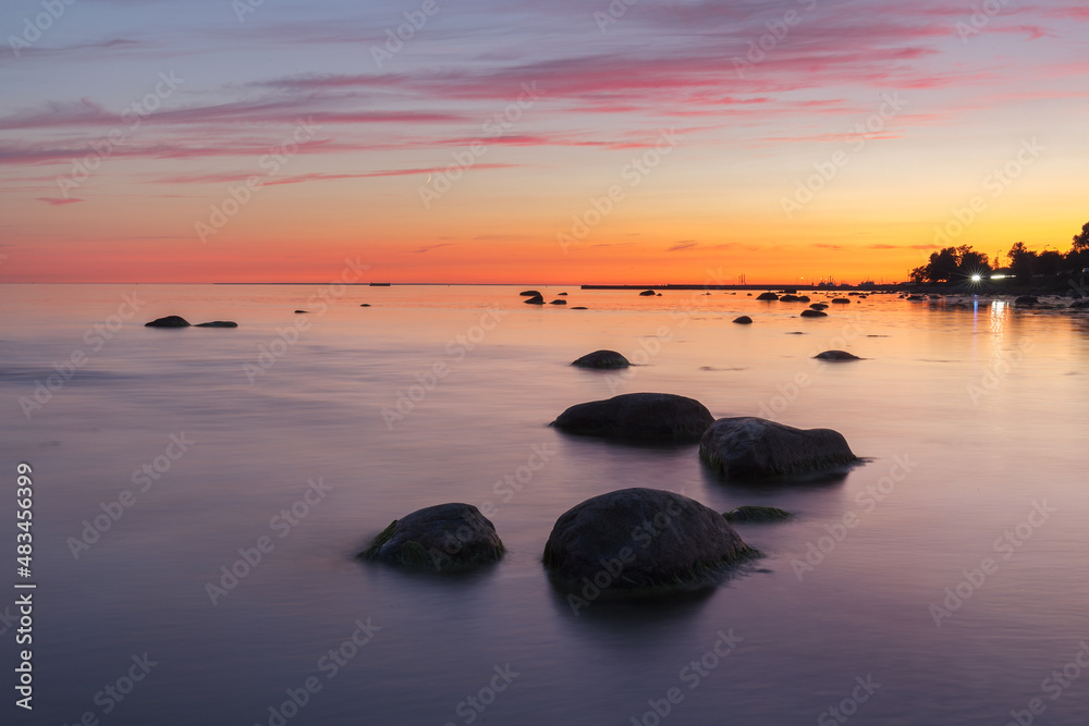 Sunset with a beutiful pink colored clouds. Long exposure photo of rocky sea shore in the evening