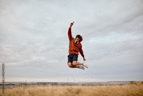 Cheerful male jumping happily, dressed in casual wear, have reat in nature in countryside. in the morning before sunrise, people active lifestyle, human emotions, sport concept. feel free and happy photo