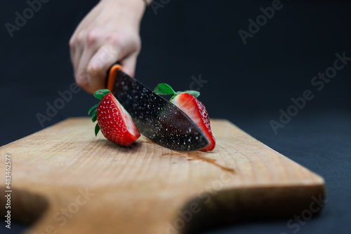 Slicing strawberry on wooden board with knife