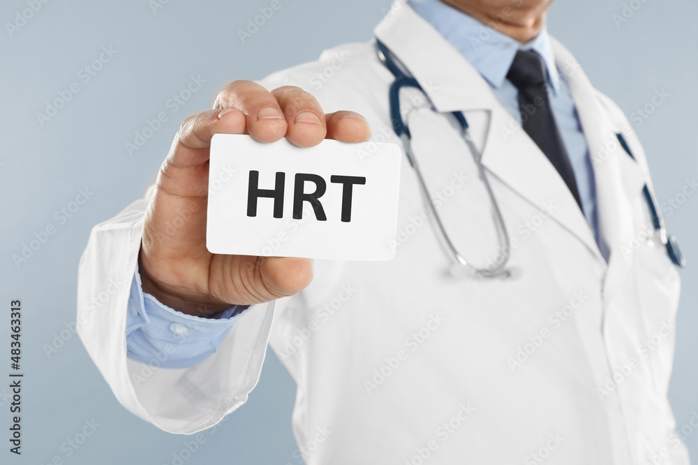 Doctor holding card with abbreviation HRT on light grey background, closeup. Hormone Replacement Therapy Doctor holding card with abbreviation HRT on light grey background, closeup. Hormone Replacement Therapy