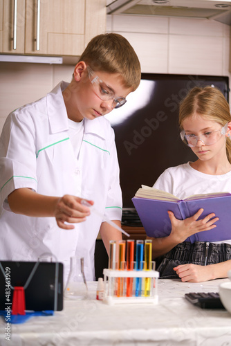 a boy mixes chemicals in a test tube at home in the kitchen. Online training. A white girl is doing a chemical experiment at home. The white boy is studying online. Home laboratory. 