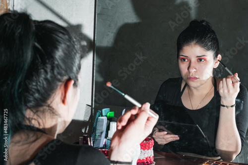 beautiful latin woman in front of her dressing table, with her gaze fixed on her made-up eyes, observing if her make-up is well done. with a brush in her right hand. concept of beauty and cosmetics. photo