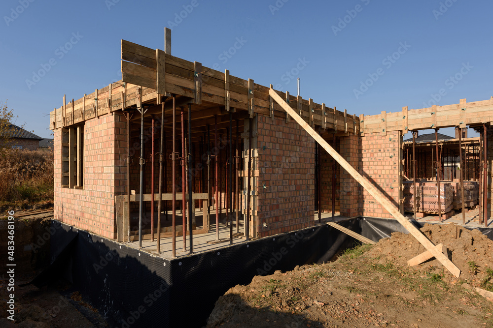 Brick house under construction. Elements of wooden formwork for pouring concrete at a construction site. Mounting telescopic stand for the installation of formwork beams.
Monolithic building.
