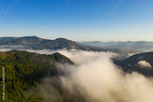 Aerial view of beautiful mountain forest covered with fluffy clouds. Drone photography