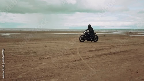 А man on a black motorcycle rides on a sandy beach.