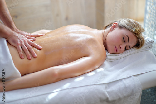 Back spine of caucasian young female having aromatherapy massage with essential oil, deep tissue massage, hands giving traditional massage in wellness beauty spa, close up, indoor shot