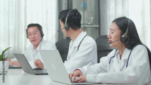 A Woman Of Three Asian Doctors With Stethoscopes Wearing Headsets Working As Call Center Agent Is Tired Because Her Colleagues Are Talking During Working At The Office
 photo