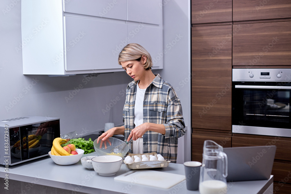 Female in kitchen during cooking biscuits, mixing dough in bowl, holidays at home. Attractive short haired female in casual shirt enjoying baking cooking, pretty housewife engaged in cooking Female in kitchen during cooking biscuits, mixing dough in bowl, holidays at home. Attractive short haired female in casual shirt enjoying baking cooking, pretty housewife engaged in cooking