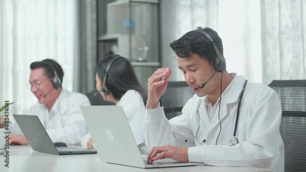A Man Of Three Asian Doctors With Stethoscopes Wearing Headsets Working As Call Center Agent Is Tired Due To Working While His Colleagues Are Talking During Working At The Office
A Man Of Three Asian Doctors With Stethoscopes Wearing Headsets Working As Call Center Agent Is Tired Due To Working While His Colleagues Are Talking During Working At The Office