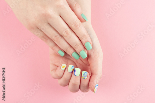 Female hands with stylish manicure closeup. Colorful abstract nail art on pink background.	