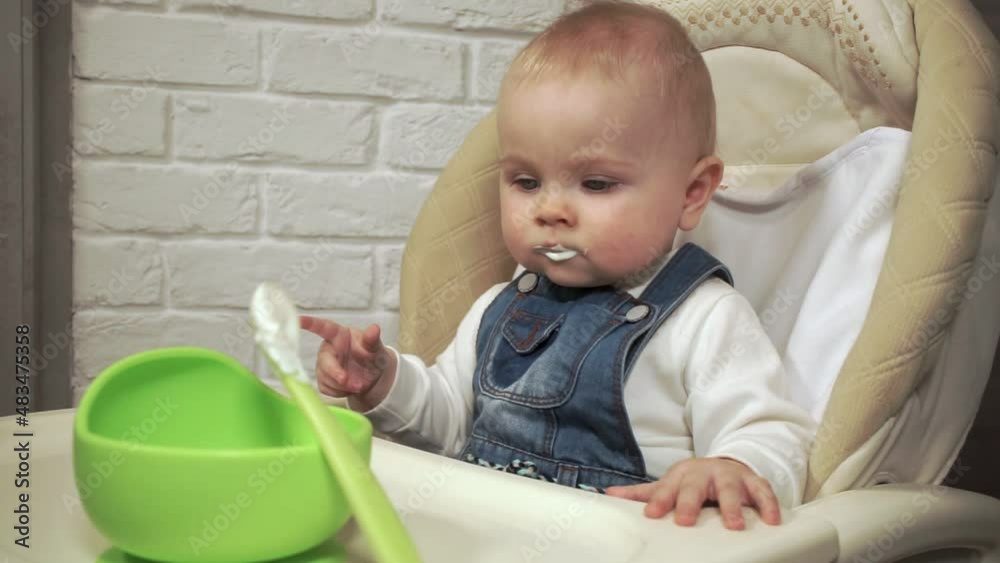 baby sits and looks at cup of food, then takes spoon and starts to eat herself baby sits and looks at cup of food, then takes spoon and starts to eat herself