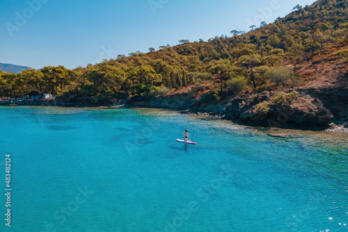 Woman stand up paddle boarding SUP on quiet sea, warm summer activity in nature, beach sport