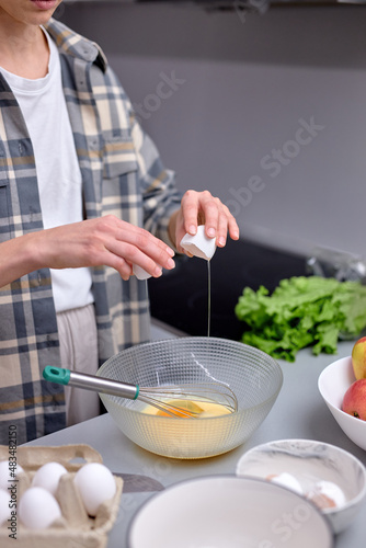 Housewife is cooking food for family, breaking egg for baking, making tasty dough , cropped unrecognizable female in casual outfit at home, in light interior kitchen. close-up hands focus