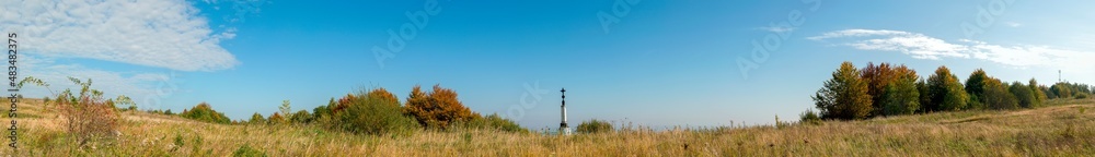 Panorama of a green field. Wooden cross. Sunny cloudless day and space.