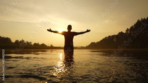 A man stands in the river with his arms open to meet the sun. The man stretched out his arms toward the sun. Calmness, wisdom, and faith with him photo
