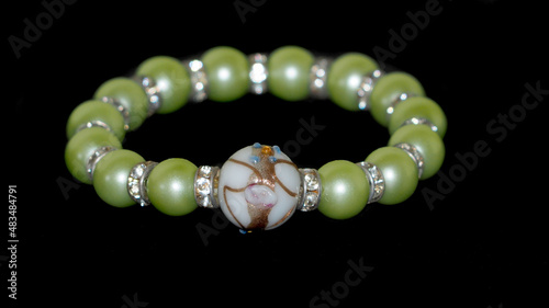 a women's bracelet made of round green beads and shiny metal inserts, a white glass ball with a Murano glass pattern on a black background. gift