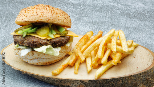 juicy cheeseburger with chili pepper, french fries, tomato, lettuce and cucumber pickle on a natural wooden tray