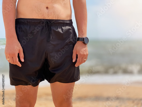 Close-up of a male torso in swimming black shorts on a beach against the background of the sea