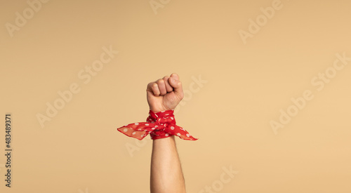 A man's hand, with a red bandana with white polka dots on his wrist, showing his fist. Feminist Movement. Beige background. photo