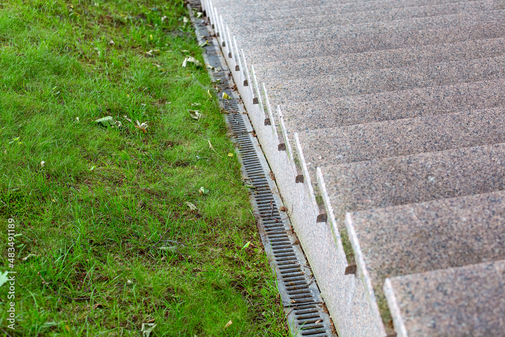 Drainage system on a slope with green grass and iron rainfall system near a granite stairs with stone steps close-up, nobody.