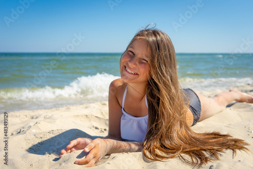 Cute little girl is sitting on the sand by the sea. Vacation.