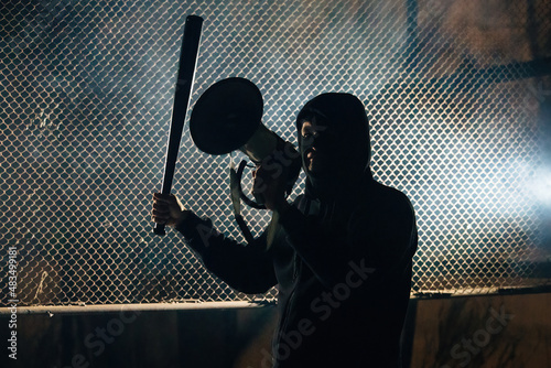 Photography Angry masked man with a bat is shouting into the megaphone