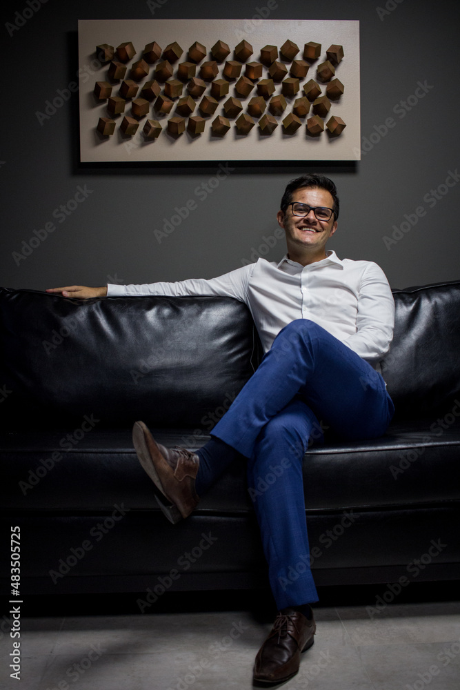 homem sorrindo sentado em sofá no seu escritório homem sorrindo sentado em sofá no seu escritório