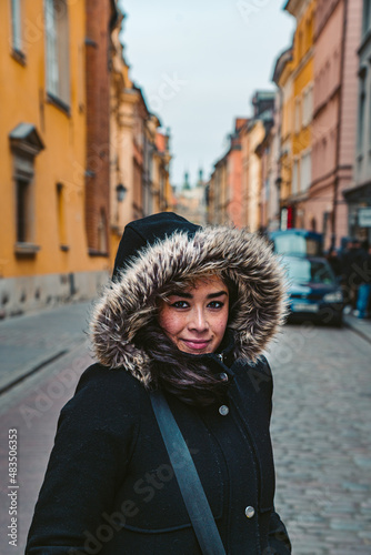Ethnic Woman Smiles in Fur Hooded Jacket on Historical European Street in Warsaw, Poland