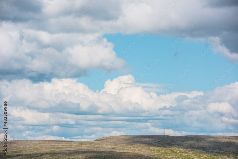 Minimalist landscape with green mountain range with sunlight and shadows from clouds at changeable weather. Minimal nature background with sunlit mountains and cloudy sky. Cumulus clouds in blue sky.