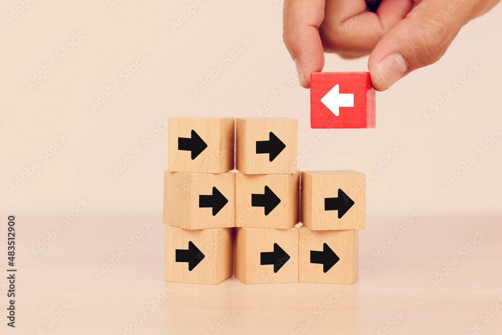 Close-up hand chooses arrow icon on cube wooden toy block stacked with pointing to opposite directions for way of adapting to change leader and transform concept.