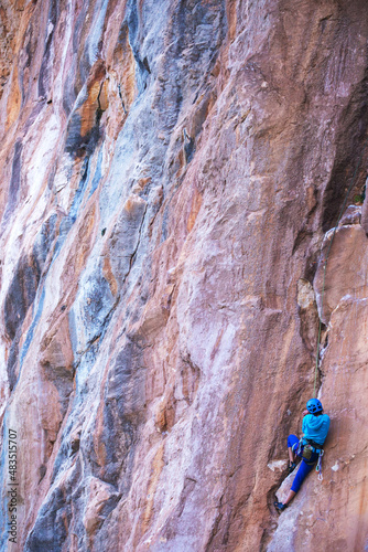 A woman in a helmet climbs a beautiful blue rock.