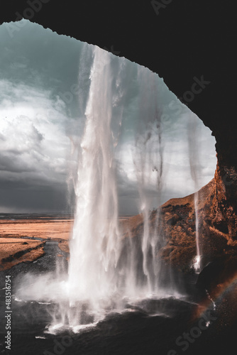 View of Seljalandsfoss from behind waterfall with a rainbow forming in Iceland photo