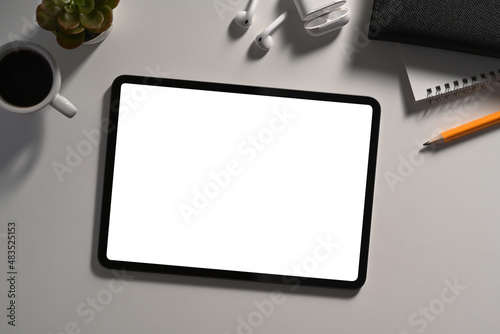 Mockup digital tablet with blank screen, wireless earphone and coffee cup on white table.