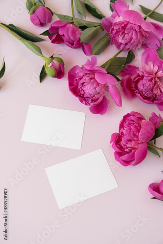 Blank paper invitation cards with copy space. Pink peony flowers bouquet on neutral pastel elegant pink background. Flat lay, top view minimal floral composition