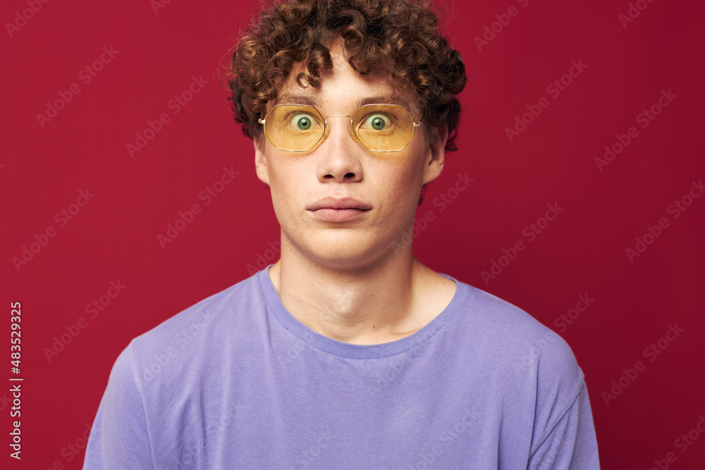 Young curly-haired man in yellow glasses purple t-shirt emotions red background Young curly-haired man in yellow glasses purple t-shirt emotions red background