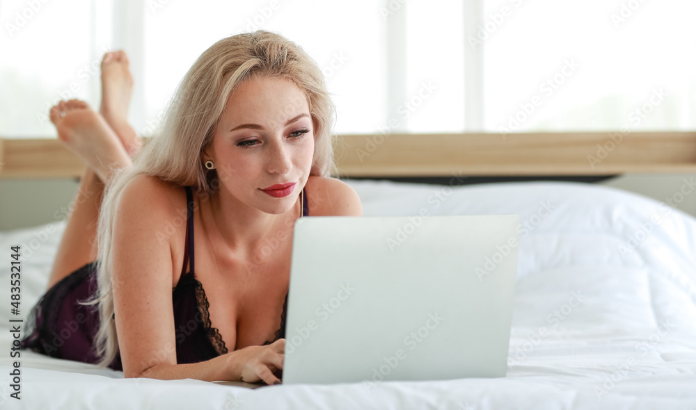 Closeup studio shot of Caucasian woman blonde hair hot female fashion model in black sexy lingerie underwear lay down smiling browsing surfing internet online via laptop on bed in bedroom Closeup studio shot of Caucasian woman blonde hair hot female fashion model in black sexy lingerie underwear lay down smiling browsing surfing internet online via laptop on bed in bedroom