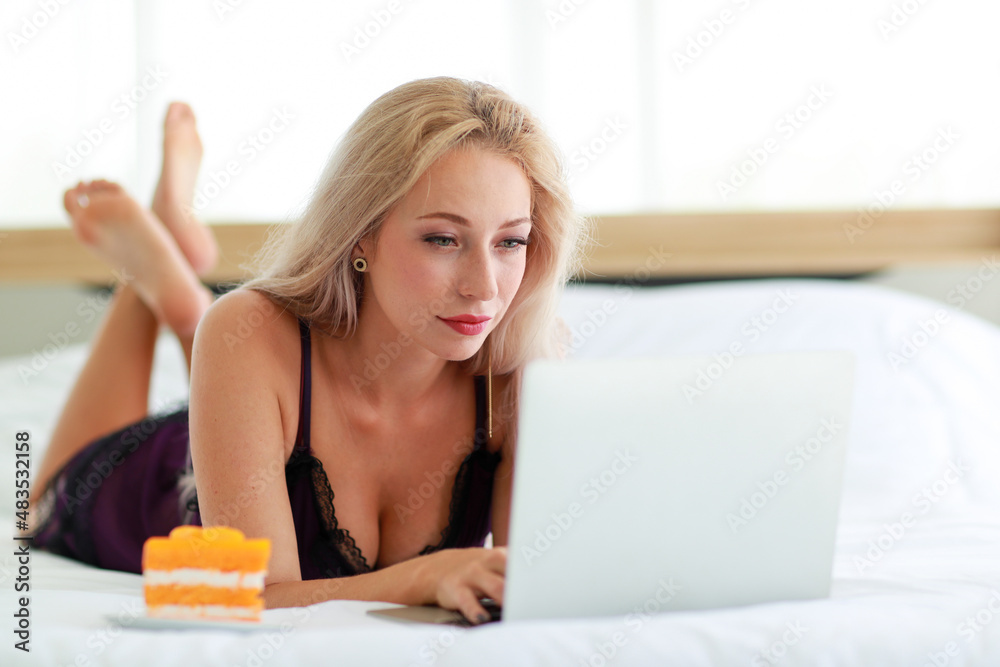 Closeup studio shot of Caucasian woman blonde hair hot female fashion model in black sexy lingerie underwear lay down smiling browsing surfing internet online via laptop eating breakfast cake Closeup studio shot of Caucasian woman blonde hair hot female fashion model in black sexy lingerie underwear lay down smiling browsing surfing internet online via laptop eating breakfast cake