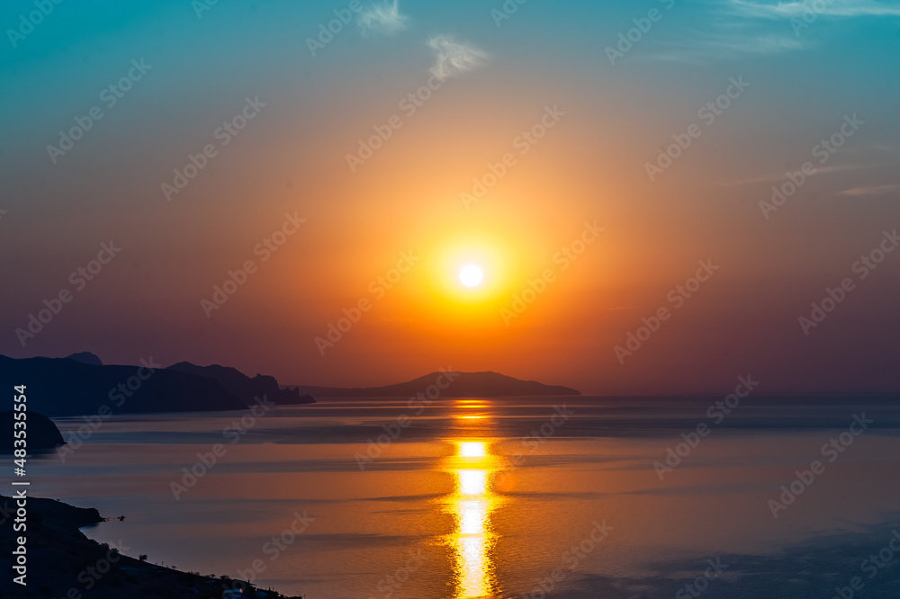 Beautiful amazing summer sunrise, bright orange colors. Cape of the mountain jutting into the sea and the reflection of the sun on the water