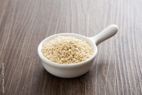 White sesame seeds in a little bowl on wooden table.