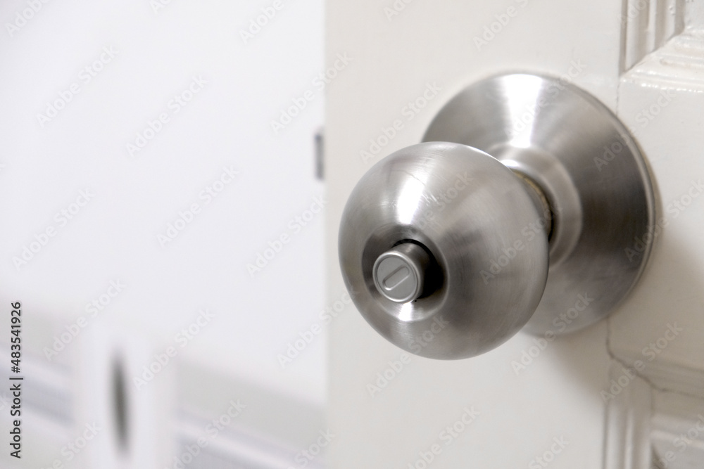 Stainless steel door knob or the handle on the wooden door In a brightly lit room. concept of cleanliness and hygiene.