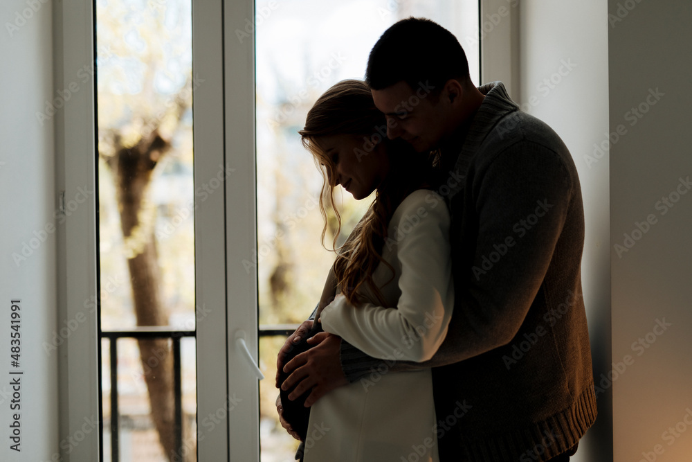 Beautiful pregnant woman and her handsome husband are hugging and smiling while spending time together Beautiful pregnant woman and her handsome husband are hugging and smiling while spending time together
