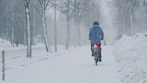 The cyclist moving on the city street during the strong snow blizzard. Finland