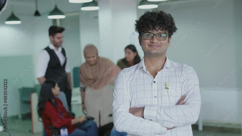 Smiling confident young pretty Indian man looking at camera standing at office home in apartment arms crossed.Portrait of young successful business man standing in office. Smiling confident young pretty Indian man looking at camera standing at office home in apartment arms crossed.Portrait of young successful business man standing in office.