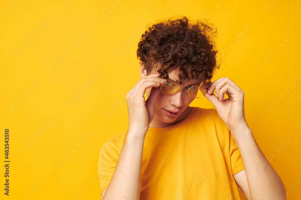Young curly-haired man Youth style glasses studio casual wear yellow background unaltered