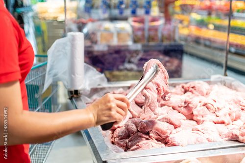 A woman holds and looks at fresh pork to buy quality pieces at the fresh produce section of the supermarket. Close up, Selective focus, Blurred background, Copy space for text or design.