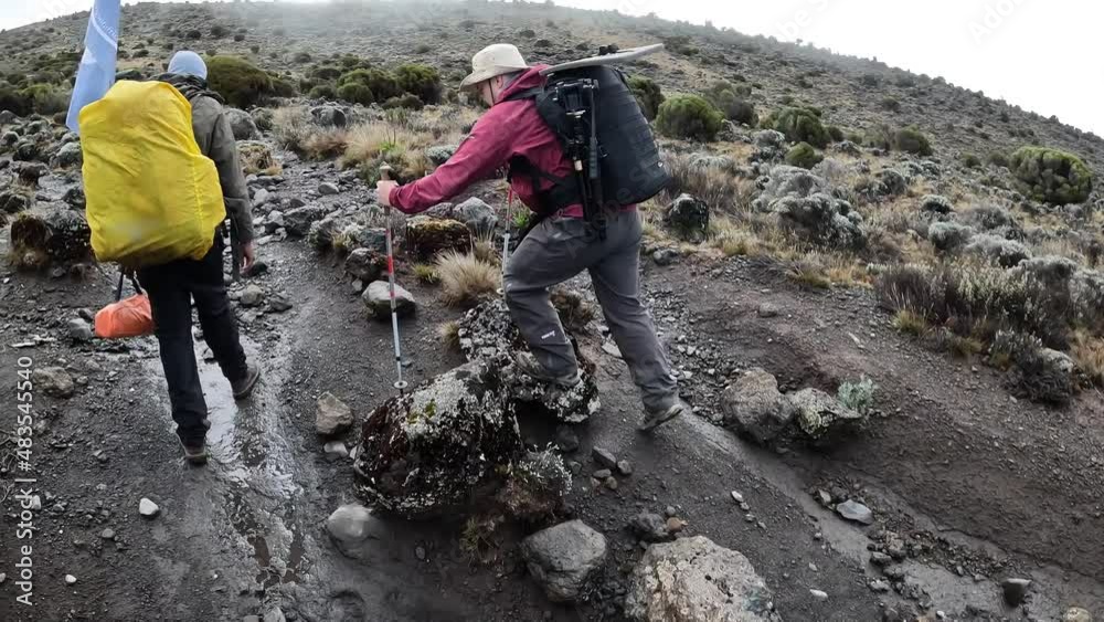 Guy tourist overtakes his guide and goes ahead. Mountain landscape. Climbing Kilimanjaro, Tanzania, Africa. Guy tourist overtakes his guide and goes ahead. Mountain landscape. Climbing Kilimanjaro, Tanzania, Africa.