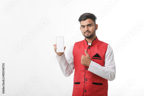Young indian man in tradition wear and showing smartphone screen on white background.