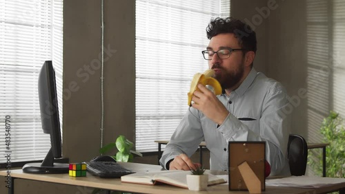 Busy casual young businessman eating banana at office desk